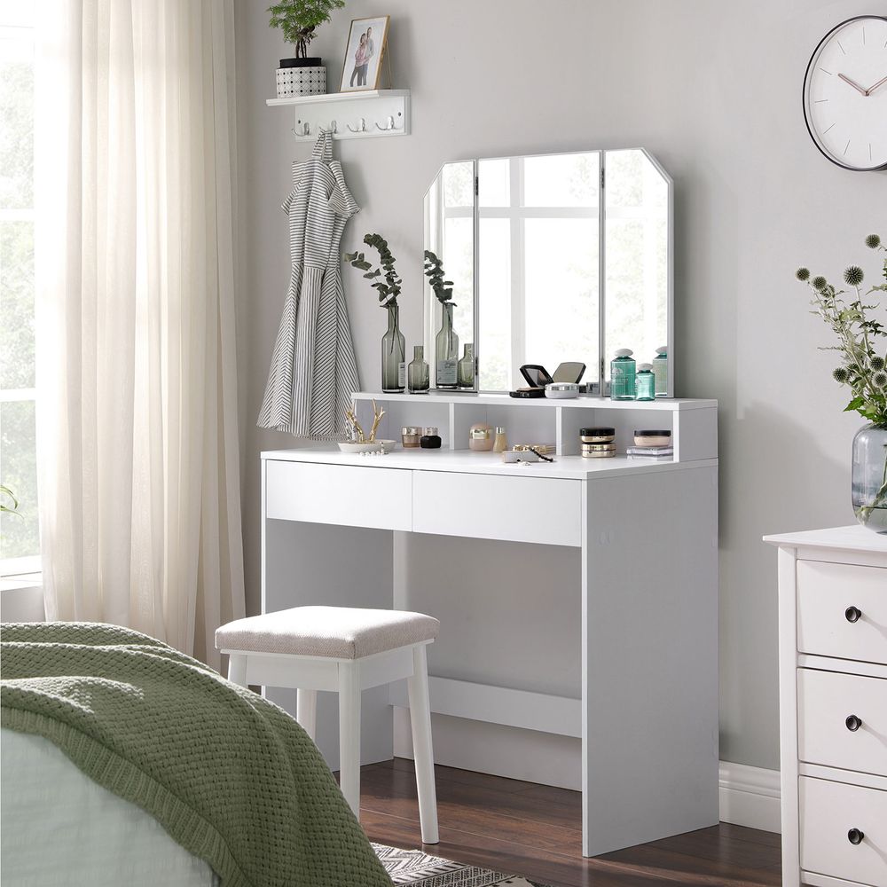 Classy white makeup dresser featuring a tri-fold mirror, two large drawers for cosmetics, three open compartments for nail polish, and a raised shelf for perfumes. Made with stain-resistant chipboard and melamine coating for durability and easy maintenance.